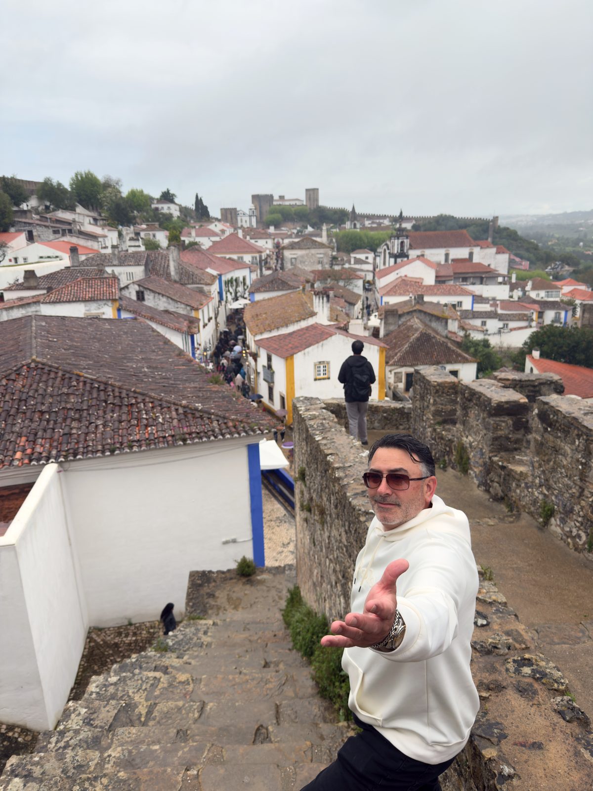 Artie on a castle wall above an old town, reaching a hand out toward the camera